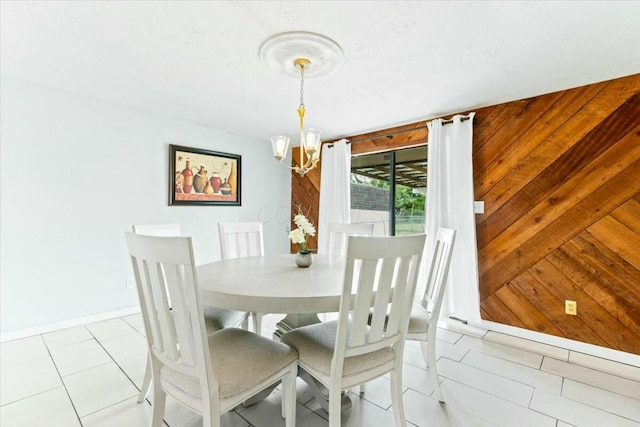 dining area featuring light tile patterned floors, wooden walls, and a chandelier