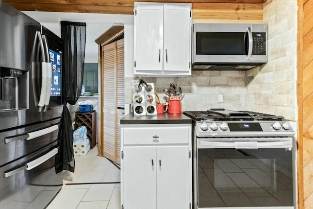 kitchen with stainless steel appliances, light tile patterned floors, white cabinets, and decorative backsplash