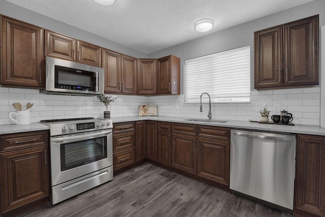 kitchen with dark hardwood / wood-style floors, sink, backsplash, stainless steel appliances, and light stone countertops