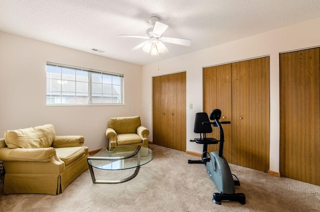 workout area with ceiling fan, light colored carpet, and a textured ceiling