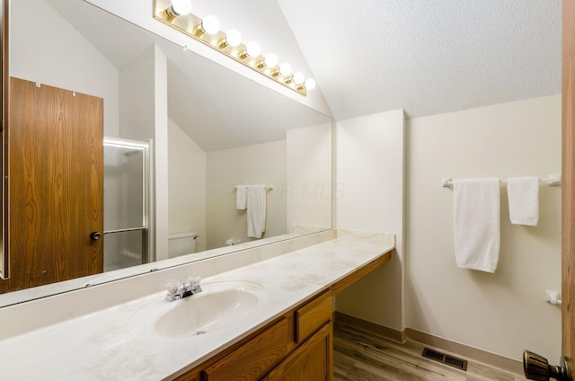 bathroom with lofted ceiling, vanity, wood-type flooring, a shower with shower door, and toilet