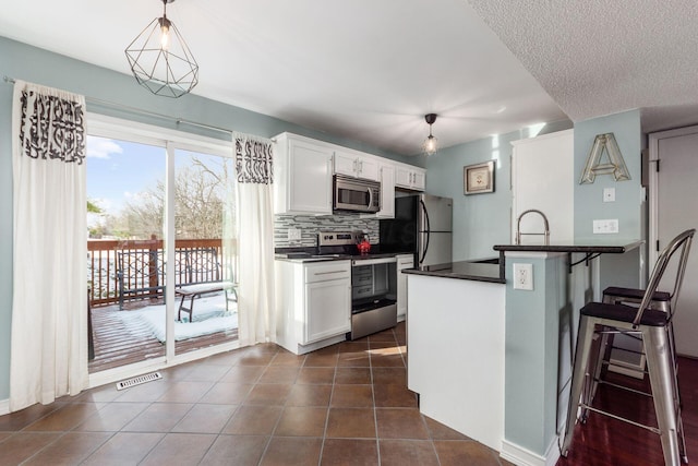 kitchen featuring a breakfast bar area, white cabinetry, decorative light fixtures, kitchen peninsula, and stainless steel appliances