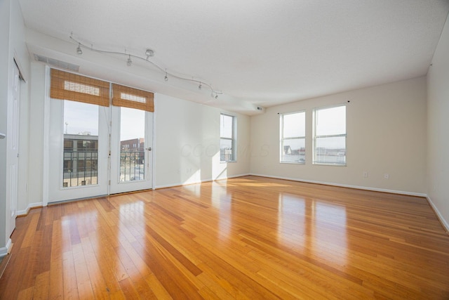 spare room with rail lighting, a textured ceiling, and light hardwood / wood-style floors