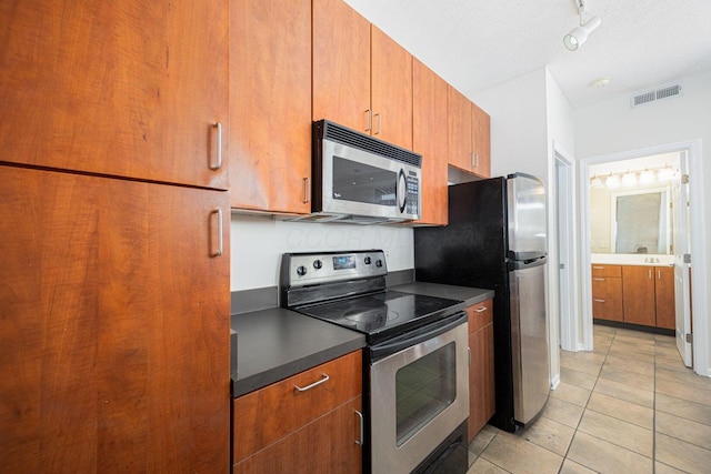 kitchen with track lighting, stainless steel appliances, a textured ceiling, and light tile patterned floors