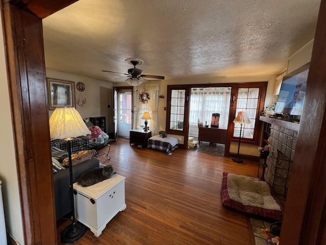 living room featuring ceiling fan, a brick fireplace, hardwood / wood-style floors, and a textured ceiling