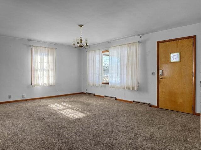 carpeted empty room featuring plenty of natural light and a chandelier