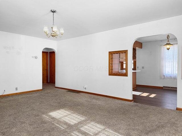 empty room featuring dark colored carpet, a chandelier, and a baseboard heating unit