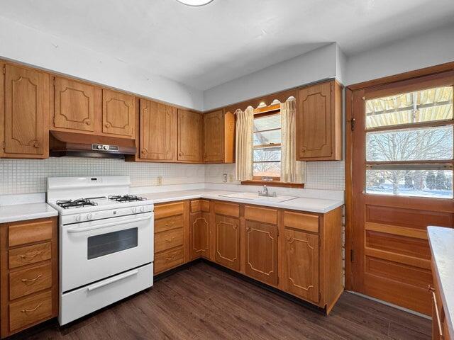 kitchen with dark wood-type flooring, white range with gas cooktop, sink, and decorative backsplash