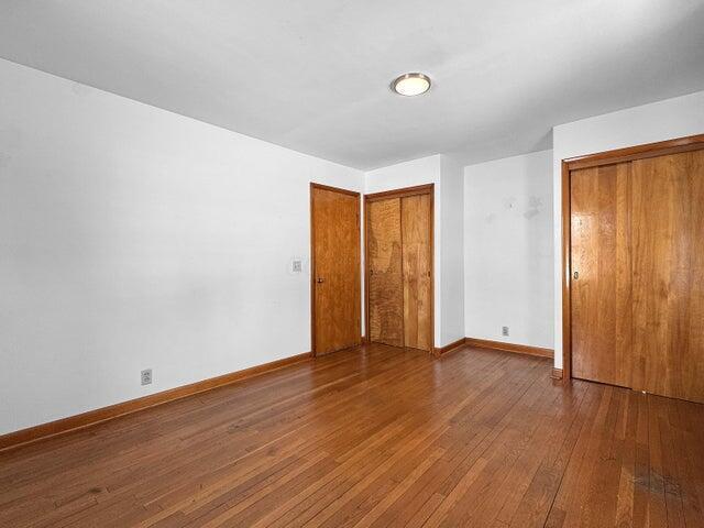 unfurnished bedroom with hardwood / wood-style flooring and multiple closets