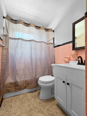 full bathroom featuring tile walls, vanity, toilet, and shower / bath combo