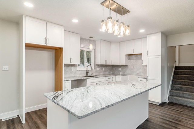 kitchen featuring hanging light fixtures, white cabinetry, a center island, and sink