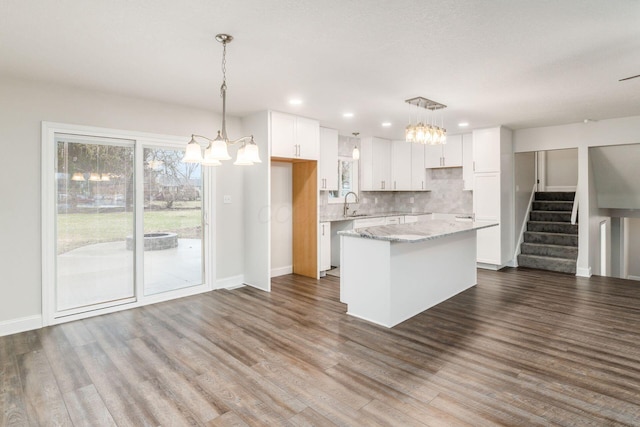 kitchen with light stone countertops, white cabinetry, a kitchen island, and decorative light fixtures