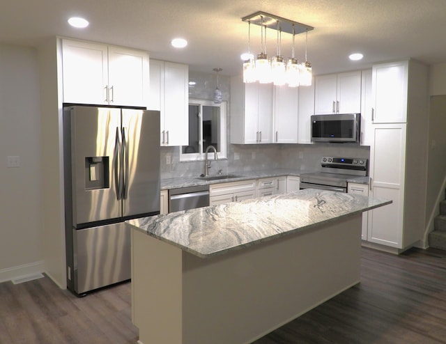 kitchen with a kitchen island, appliances with stainless steel finishes, white cabinets, and light stone counters