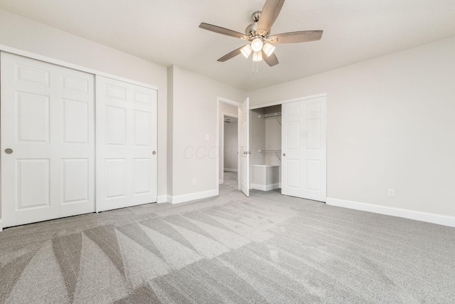 unfurnished bedroom with two closets, light carpet, and ceiling fan