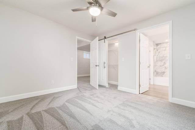 bedroom with ceiling fan, connected bathroom, a barn door, light colored carpet, and a closet