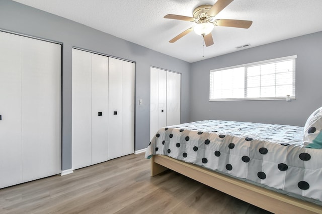 bedroom with two closets, visible vents, light wood-style flooring, a ceiling fan, and a textured ceiling