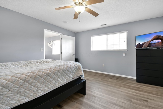 bedroom featuring visible vents, a textured ceiling, baseboards, and wood finished floors