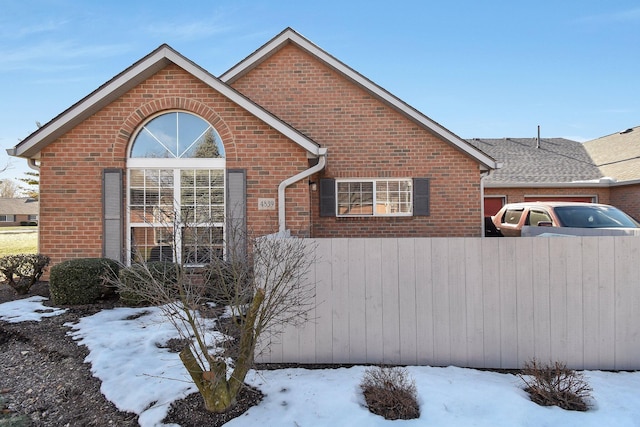 snow covered property featuring fence and brick siding