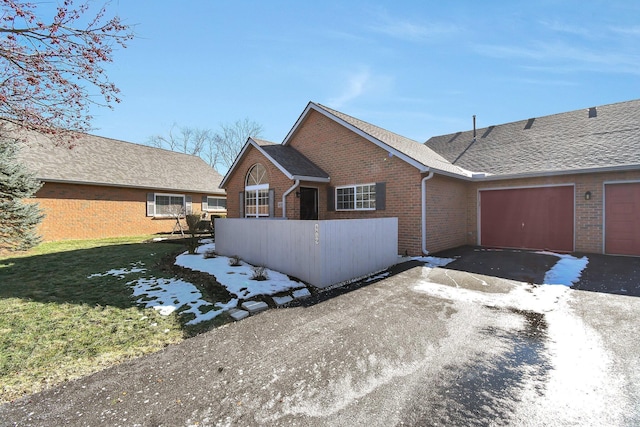 view of front facade with a lawn, aphalt driveway, roof with shingles, an attached garage, and brick siding