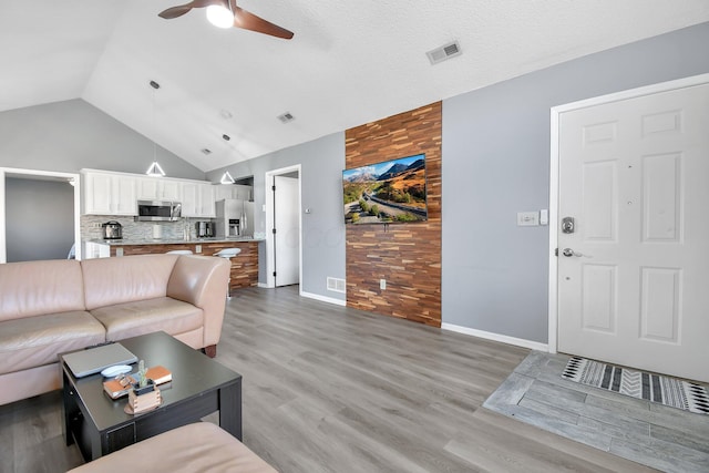 living room featuring lofted ceiling, light wood-type flooring, visible vents, and ceiling fan