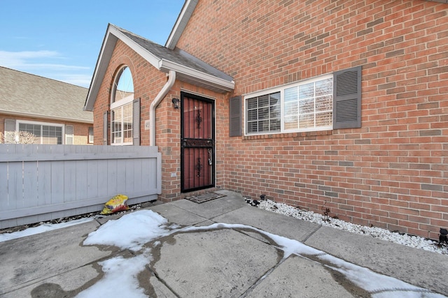 snow covered property entrance with brick siding and fence