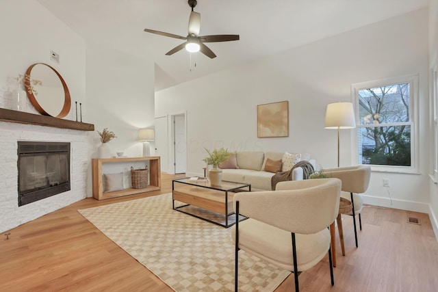 living room featuring a stone fireplace, ceiling fan, and light wood-type flooring