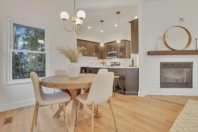 dining room featuring a notable chandelier, a fireplace, and light wood-type flooring