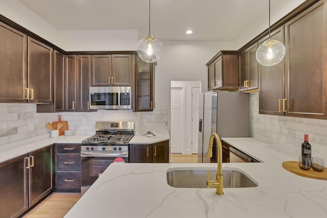 kitchen featuring appliances with stainless steel finishes, pendant lighting, sink, dark brown cabinetry, and light stone counters