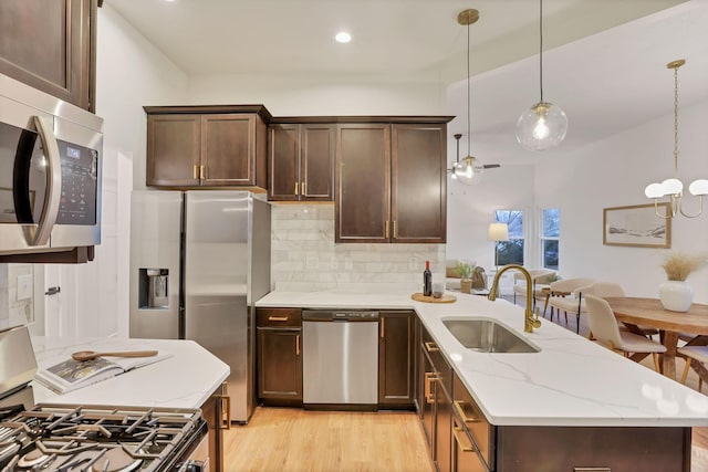 kitchen featuring sink, stainless steel appliances, light stone countertops, decorative light fixtures, and light wood-type flooring