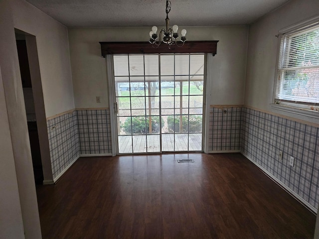 spare room featuring dark wood-type flooring, a chandelier, wainscoting, and wallpapered walls