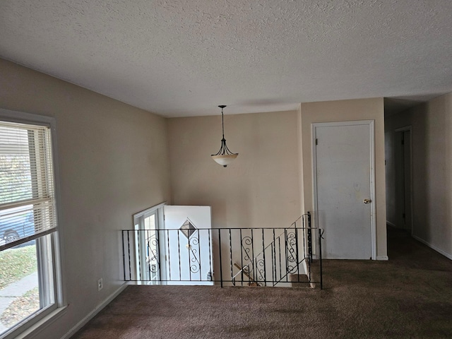 hall featuring baseboards, dark carpet, a textured ceiling, and an upstairs landing