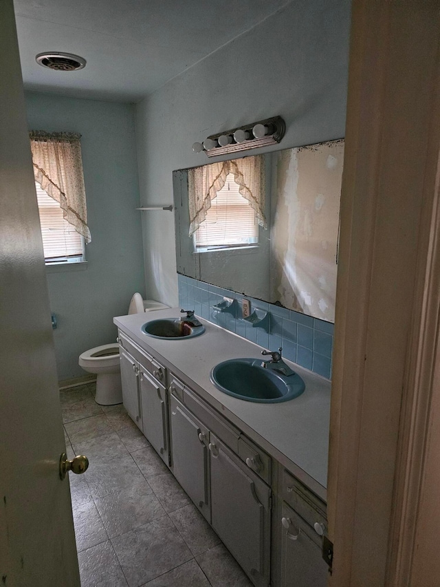 bathroom with toilet, double vanity, decorative backsplash, and a sink