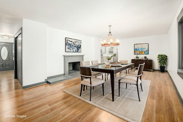 dining space featuring an inviting chandelier, a brick fireplace, and light hardwood / wood-style flooring