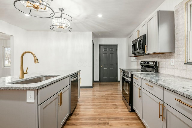 kitchen with sink, gray cabinetry, hanging light fixtures, stainless steel appliances, and an island with sink