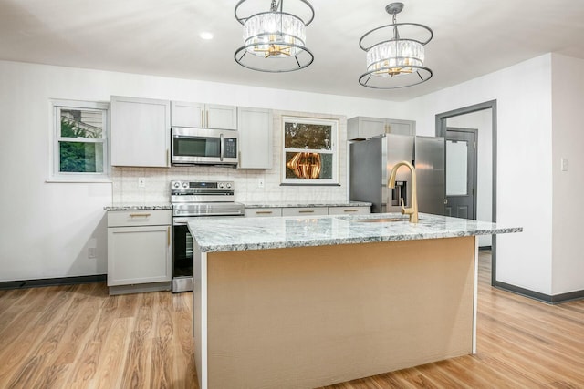 kitchen featuring a chandelier, hanging light fixtures, an island with sink, stainless steel appliances, and light stone countertops