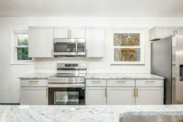 kitchen with light stone countertops, appliances with stainless steel finishes, and decorative backsplash