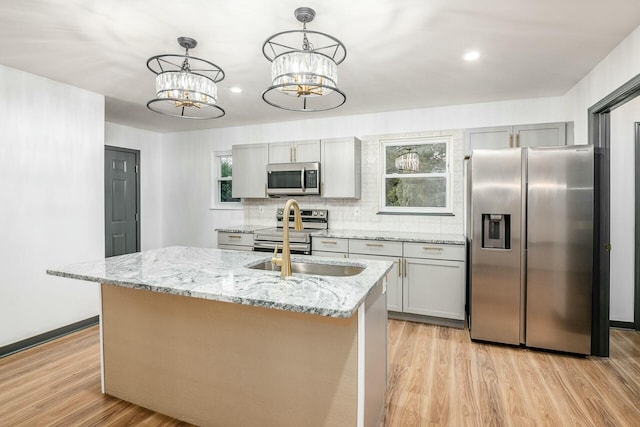 kitchen with gray cabinetry, stainless steel appliances, hanging light fixtures, and a center island with sink