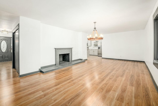 unfurnished living room with a brick fireplace, a chandelier, and light wood-type flooring