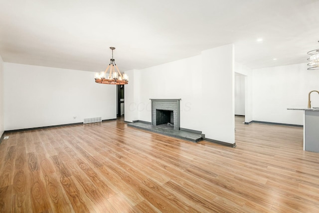 unfurnished living room with a brick fireplace, light hardwood / wood-style flooring, and a chandelier