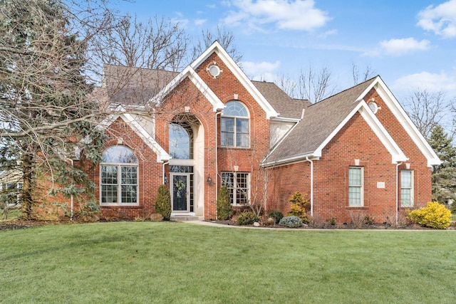 view of front of house with brick siding, a shingled roof, and a front yard