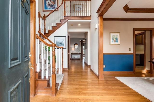 entrance foyer with light wood-style flooring, baseboards, ornamental molding, and stairway