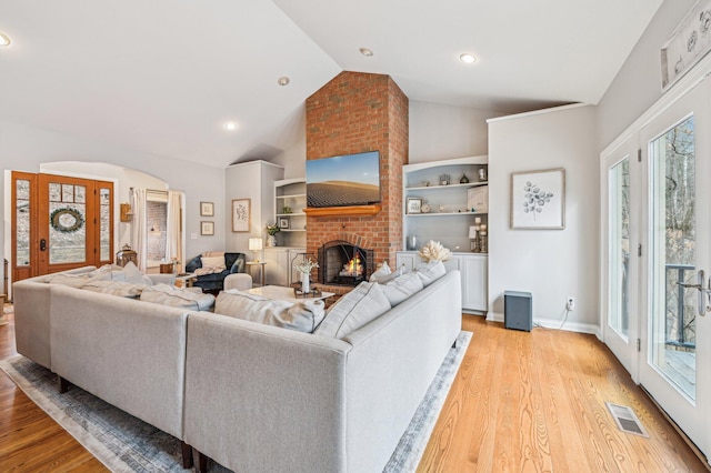 living room with lofted ceiling, a brick fireplace, and light hardwood / wood-style flooring