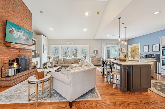 living room with sink, vaulted ceiling, light hardwood / wood-style floors, and a brick fireplace