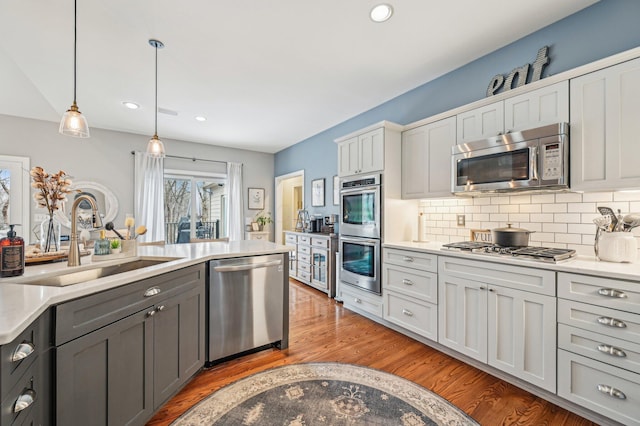 kitchen featuring sink, light hardwood / wood-style flooring, backsplash, stainless steel appliances, and decorative light fixtures