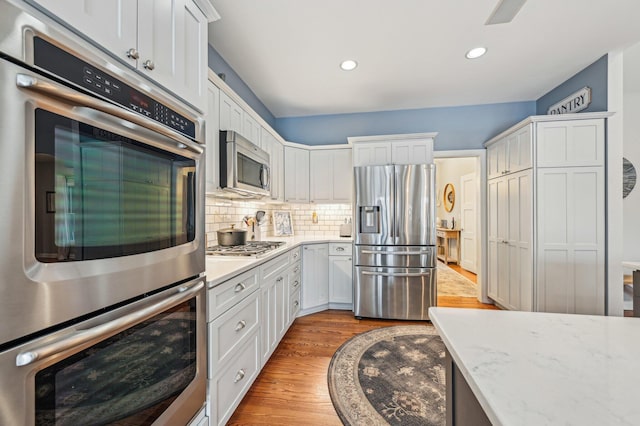 kitchen featuring white cabinetry, tasteful backsplash, light wood-type flooring, appliances with stainless steel finishes, and light stone countertops