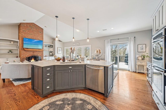 kitchen featuring pendant lighting, gray cabinetry, stainless steel appliances, a brick fireplace, and a center island with sink