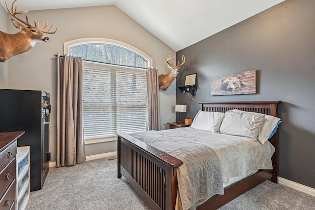 carpeted bedroom with multiple windows, vaulted ceiling, and stainless steel fridge