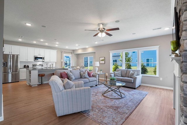 living room with a stone fireplace, light hardwood / wood-style floors, and a textured ceiling