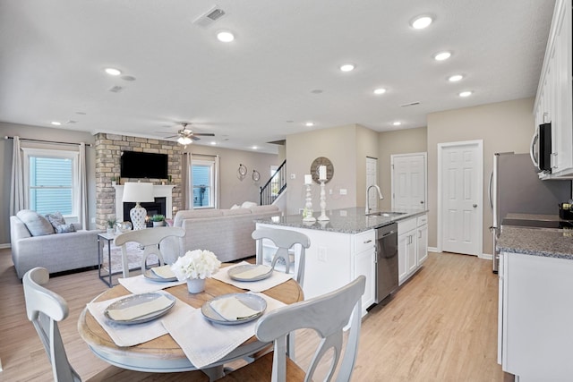 dining space with sink, a fireplace, light hardwood / wood-style floors, and ceiling fan