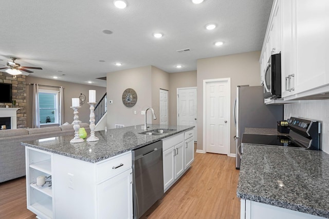 kitchen with sink, white cabinetry, a kitchen island with sink, stainless steel appliances, and a large fireplace